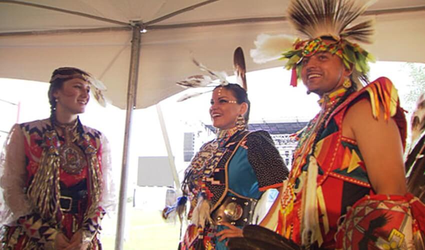 Native dancers waiting under a shaded tent.