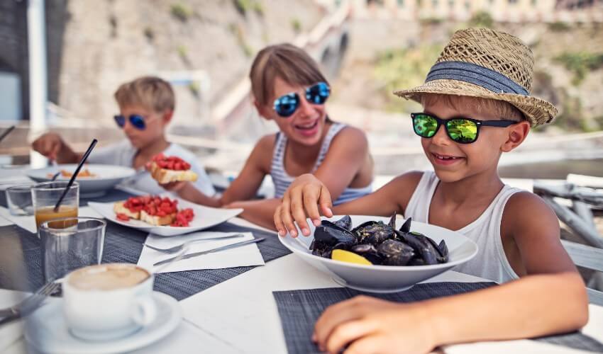 A little boy is eating mussels and his sister is having a bruschetta at an Italian restaurant.