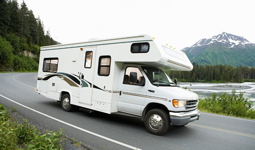 RV driving down a scenic roadway with mountains in the background.