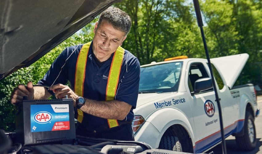 CAA Battery Service technician under car hood with a CAA battery.