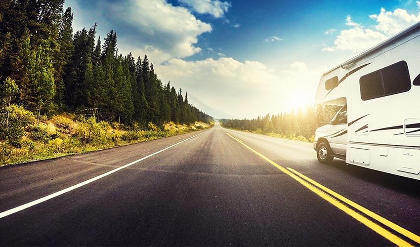 An RV vehicle driving into the sunset with a forest on the left.
