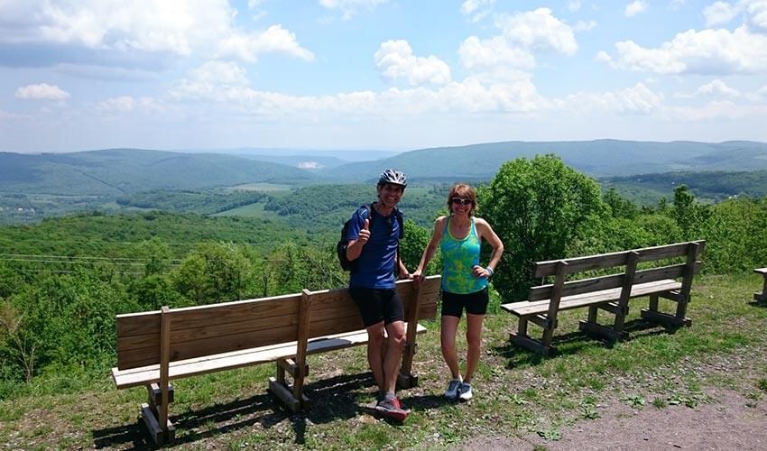 Vicky and Fernando Perez standing in behind park benches with an open, elevated view of forests and skyline.