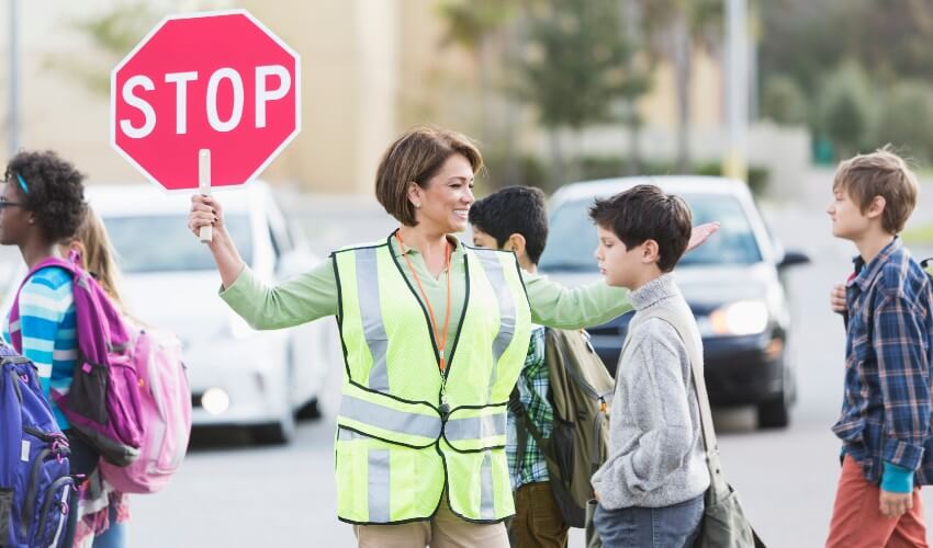 Female crossing guard helping kids cross the street.