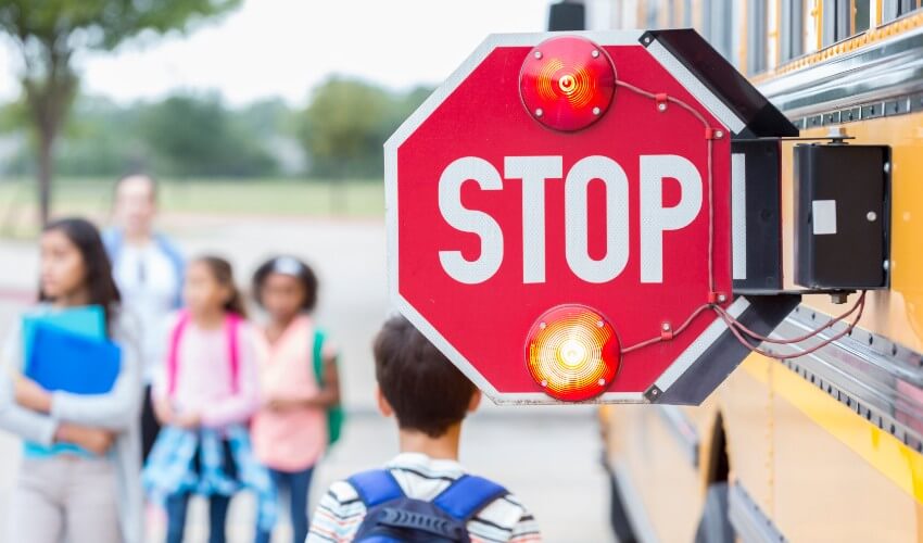 Close up of a flashing school bus stop sign with children in the background.