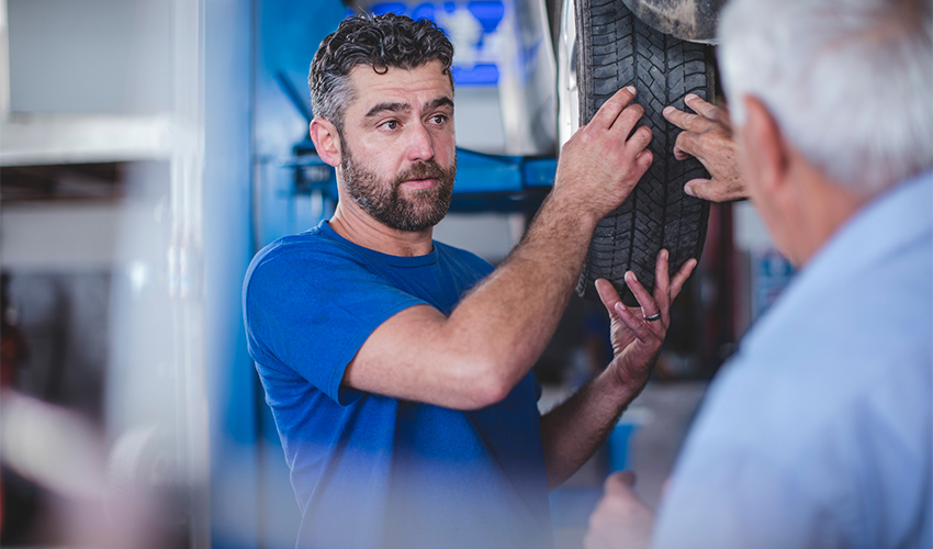 Technician showing mature man tire tread.
