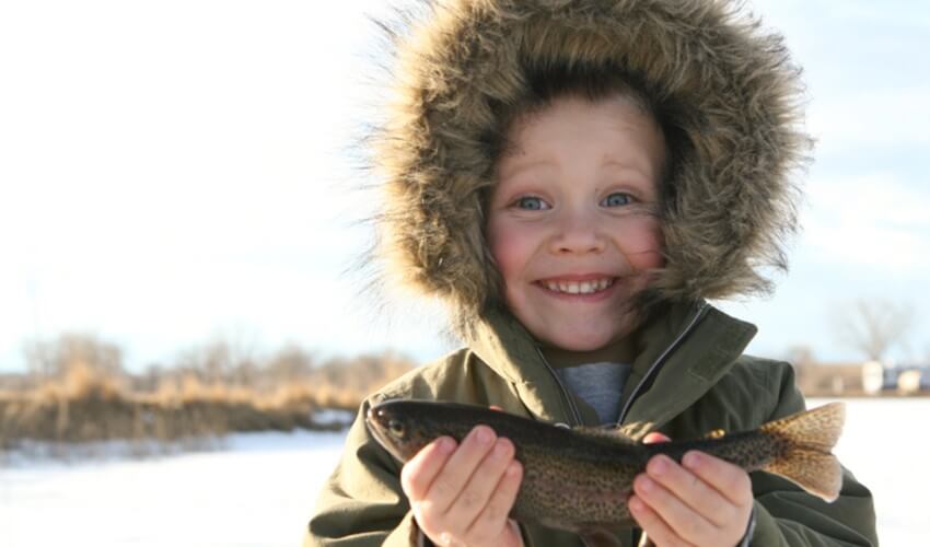 A little boy holding a fish outside on a snowy day.