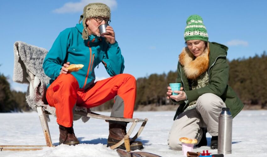 Man and woman having food while ice fishing.