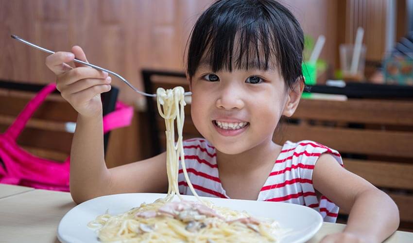 Young girl eating a plate of pasta.