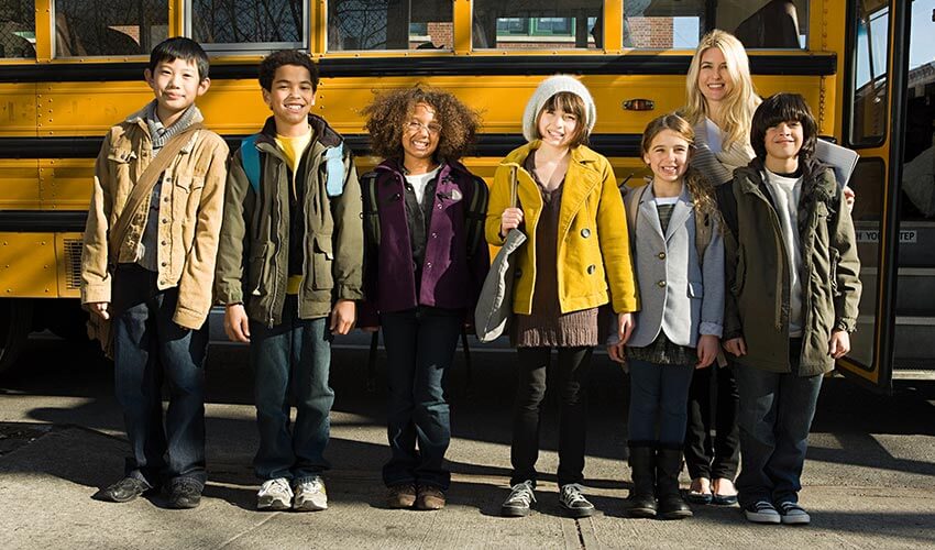 A group of students standing in front of a school bus with their teacher.