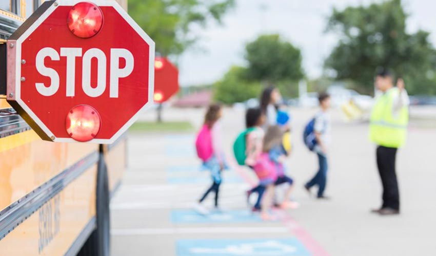 Detailed view of a stop sign on a school bus, with children crossing a screen in the background.