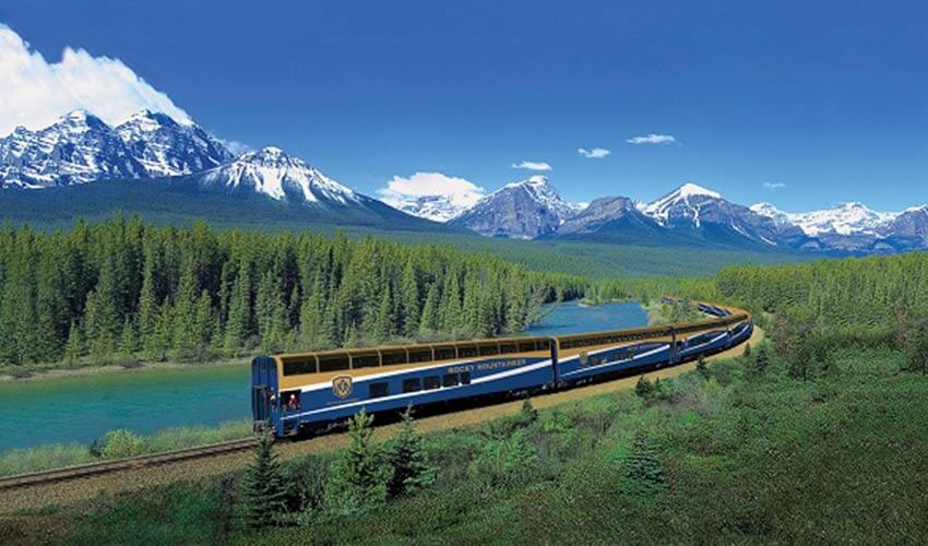 A Rocky Mountaineer train with mountains and river in the background.