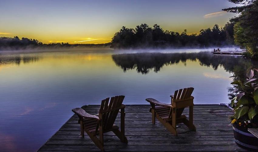 A beautiful Muskoka evening on the lake, two Muskoka chairs on a dock.