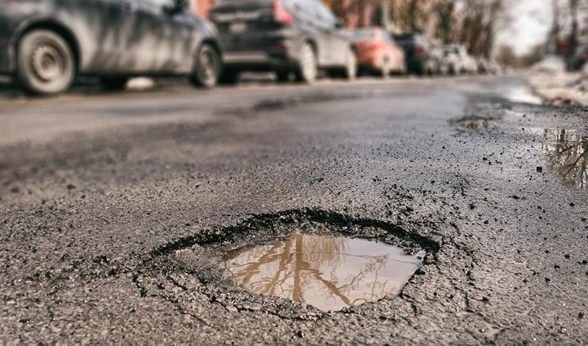 A small pothole in a street with cars parked on the side.