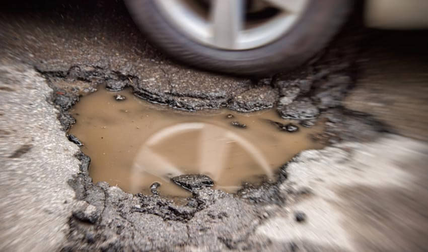 A car narrowly miss hitting a pothole.