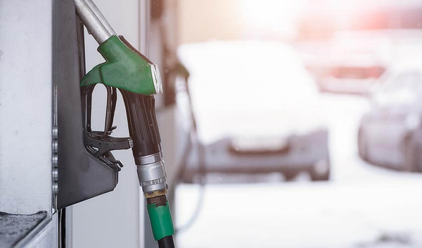 A closeup of a green gas pump with cars covered with snow in the background.