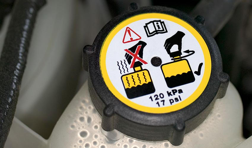 A closeup of a coolant reservoir and cap with warning label.