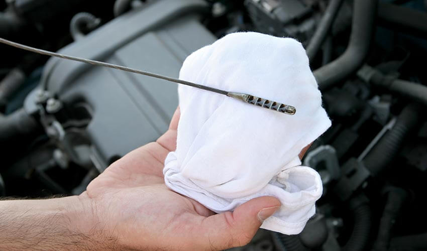 A closeup of a hand holding an engine oil dipstick.