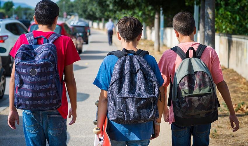 Three teenage kids wearing backpacks walking to school.