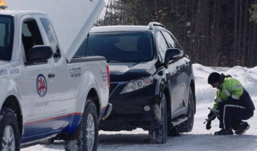 CAA driver providing roadside assistance to a black SUV in winter.