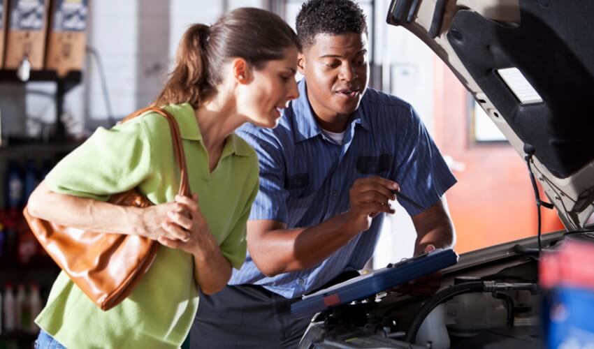 Male auto mechanic with female customer looking under the hood of a car.