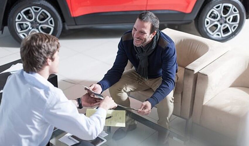 Man at car dealership looking at brochure.