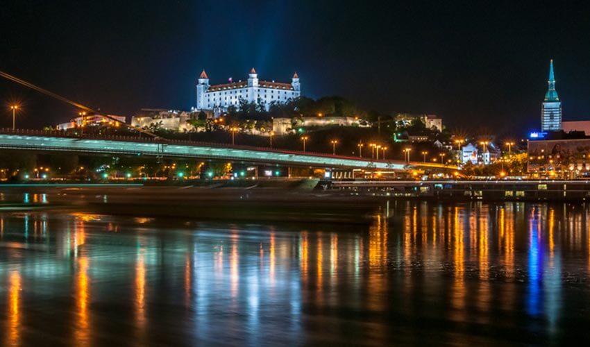 The Danube River at night with views of a bridge and the Bratislava Castle