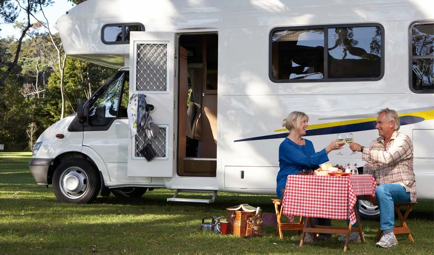 Mature couple having picnic beside motor home in park, toasting.