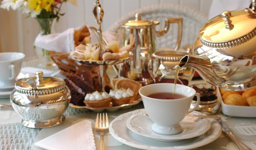 Tea being poured into a cup on a table set for afternoon tea.