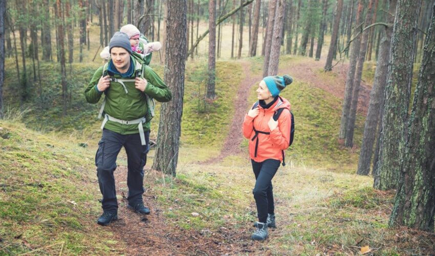 Family on a hike in the forest with a baby in a carrier on father's back.