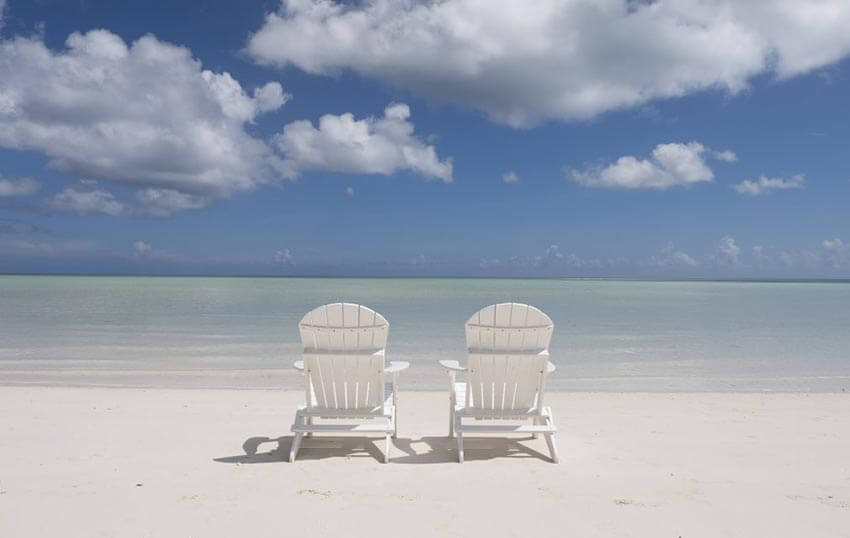 Two white beach chairs facing the clear waters at Cable Beach, Nassau.