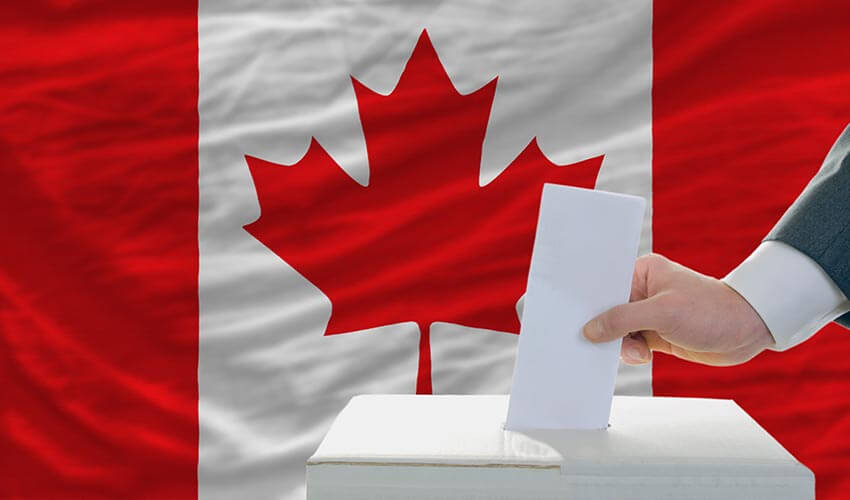 A hand putting a ballot into a box with the Canadian flag in the background.