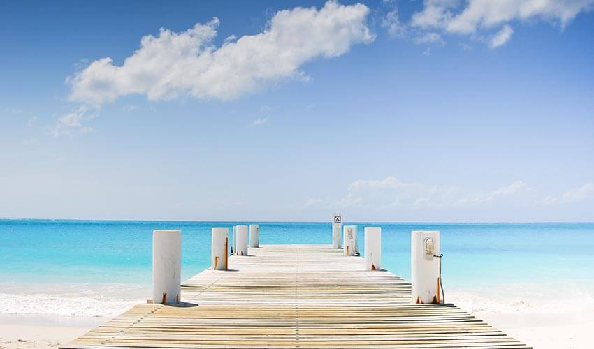 A pier leading into a pristine blue ocean and sky.