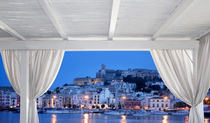 Overlooking night time waterfront scenery of Ibiza inside a cabana.