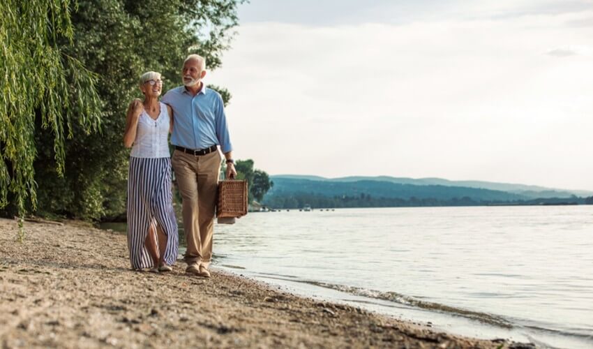An affectionate senior couple going on a picnic at the riverbank.