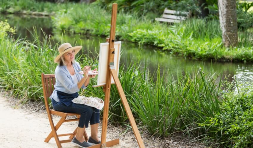 Senior woman painting a picture on canvas outdoors.