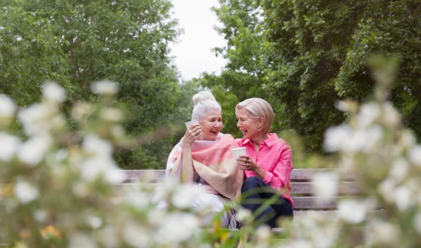 Two senior women having coffee together in park.