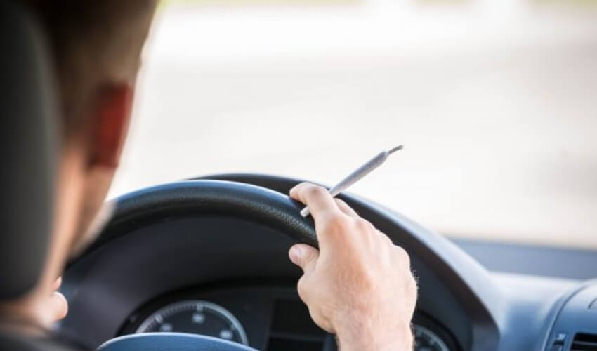 A male driver holding a rolled cannabis cigarette.
