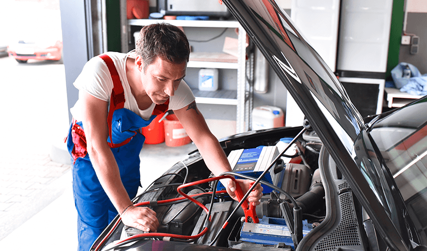 A technician working on a car, testing car battery.