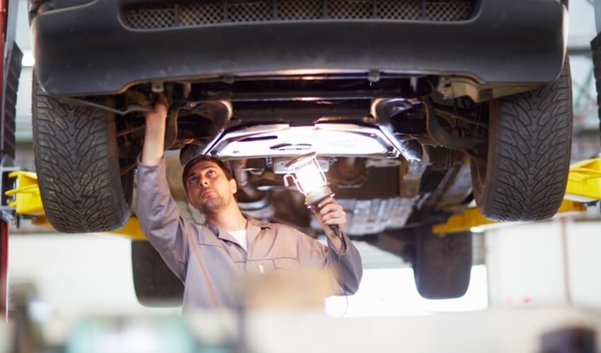 A technician looking at the underbody of a car.