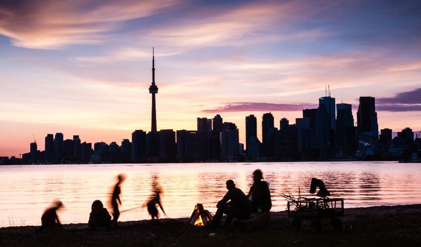 Family picnic on the shore of Toronto Island with the Toronto skyline at dusk.