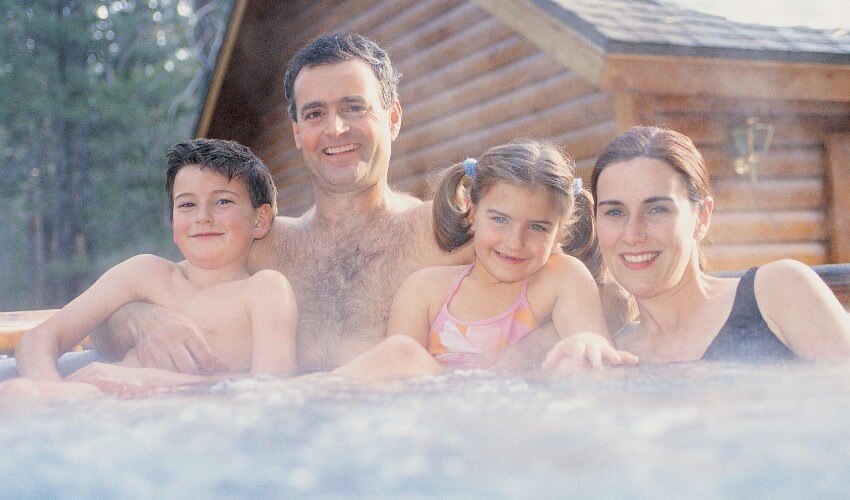 Parents and two children enjoying an outdoor hot tub.