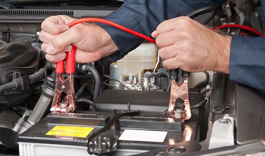 Close up of hands holding jumper cables, boosting a car battery.