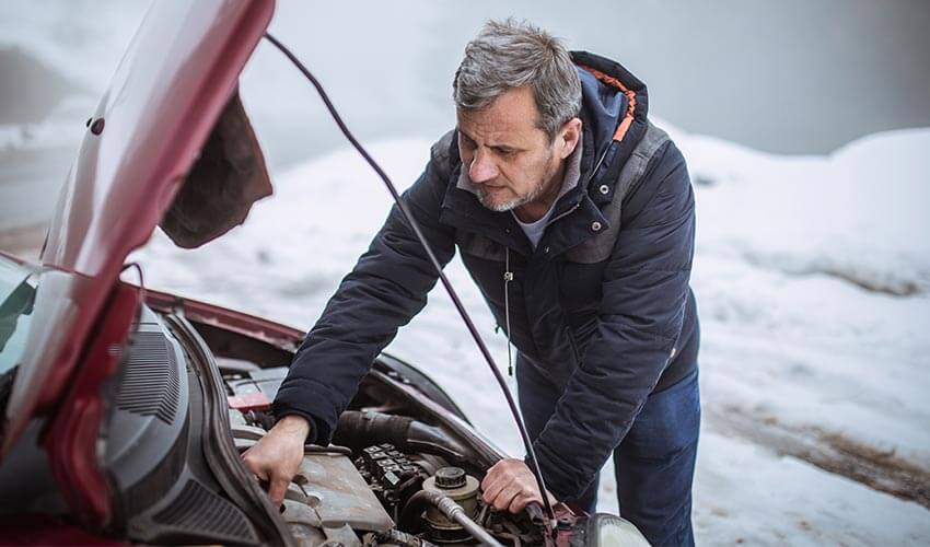 A man checking inside the hood of car in winter.