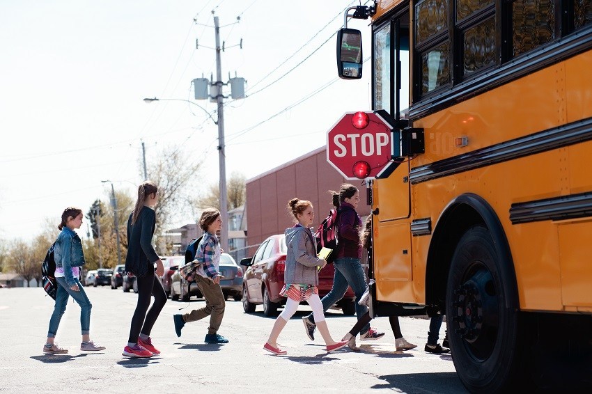 Group of elementary school kids getting in a yellow school bus at school's out. Boys and girls age 8-11. They seem happy to finish the school. Boys with bicycles are out of focus. This was taken in Quebec, Cansada.