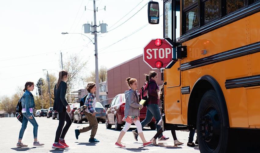 Children crossing a street in front of school bus.
