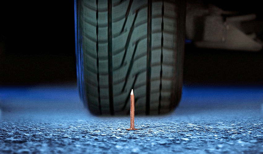 A nail in front of a car tire.