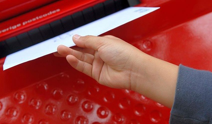 A person's hand putting an envelope into a mailbox.