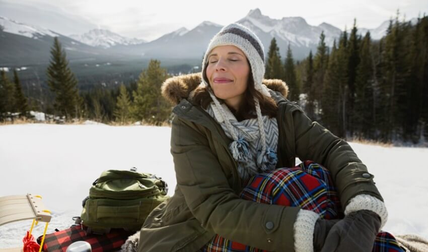 A woman with a sled resting on the snow with mountains in the background.