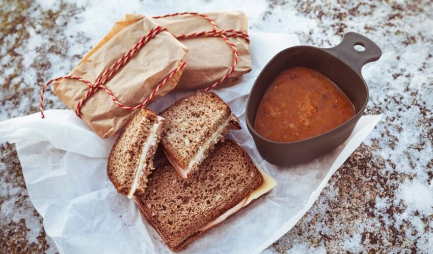 High angle view of a sandwich and soup on a snow covered field.