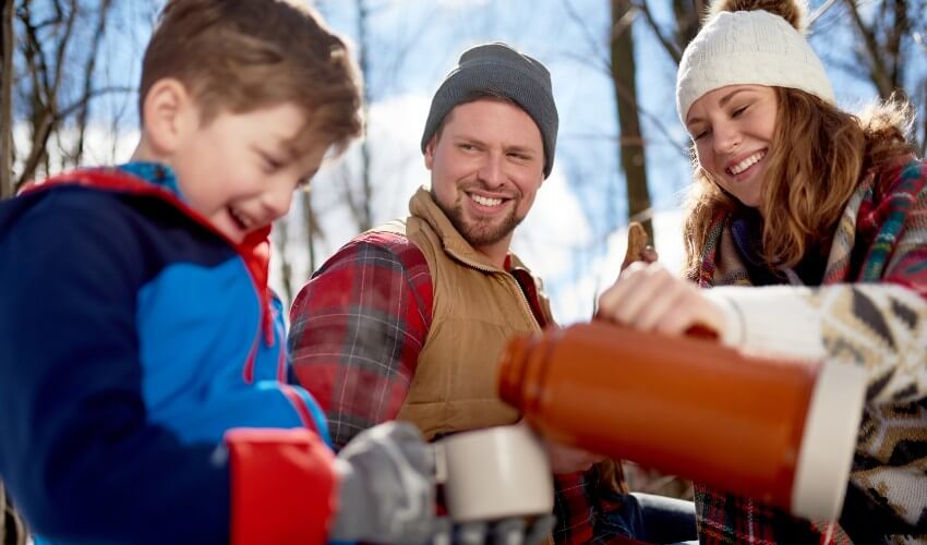 Mom, dad and son sharing a cup of cocoa and cookies outdoors in the winter.